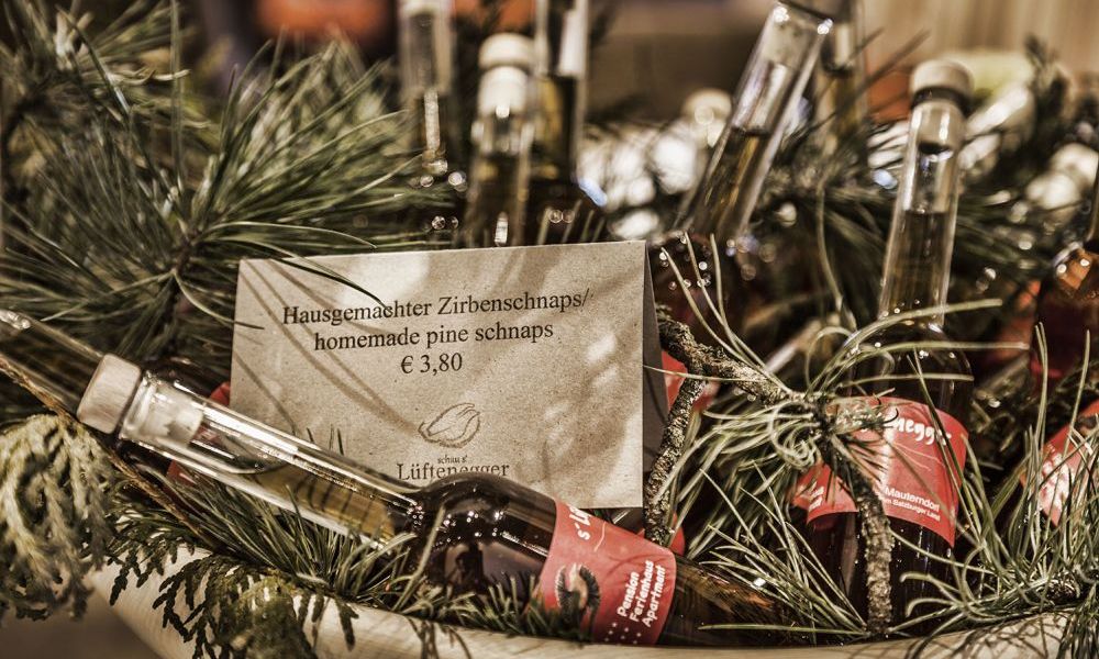 Korb mit Flaschen hausgemachtem Zirbenschnaps, umgeben von Kieferzweigen.