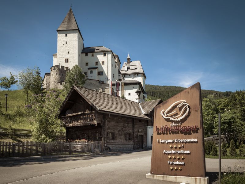 Alpenpension mit Holzfassade, Berge und Schloss im Hintergrund, Lungau, Salzburg.