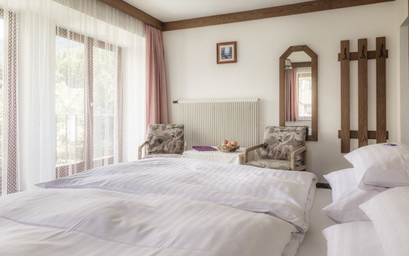 Gemütliches Familienpension-Zimmer mit Doppelbett, Sesseln und Bergblick. Helle Einrichtung und Holzakzente.