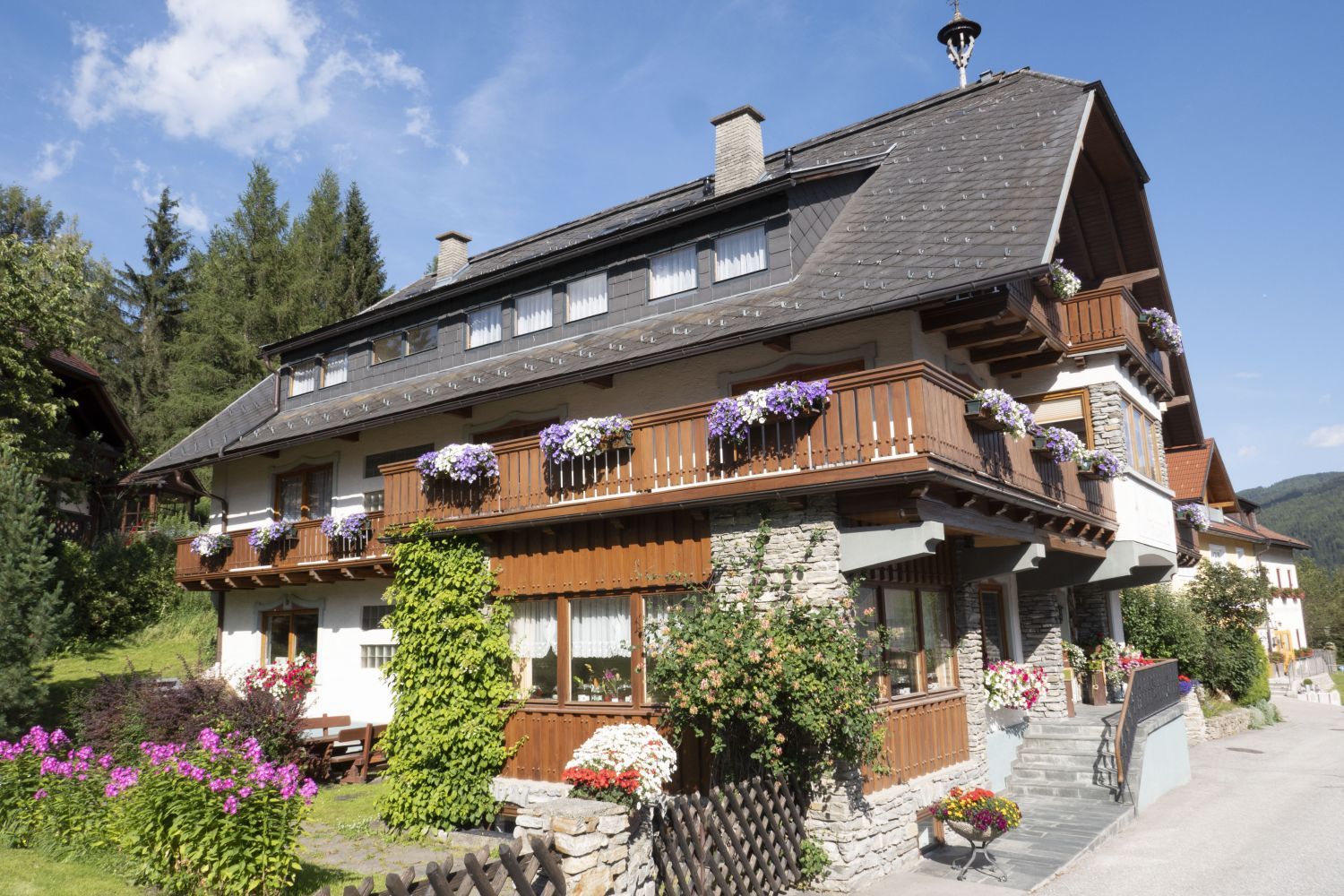 Charmante Alpenpension mit Holzbalkonen und bunten Blumen, eingebettet in die Berge des Salzburger Lungau.