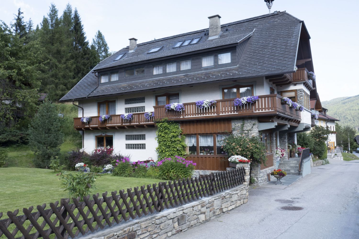 Drei-Sterne-Familienpension in Mauterndorf mit Blumenbalkonen, von Bergen umgeben.