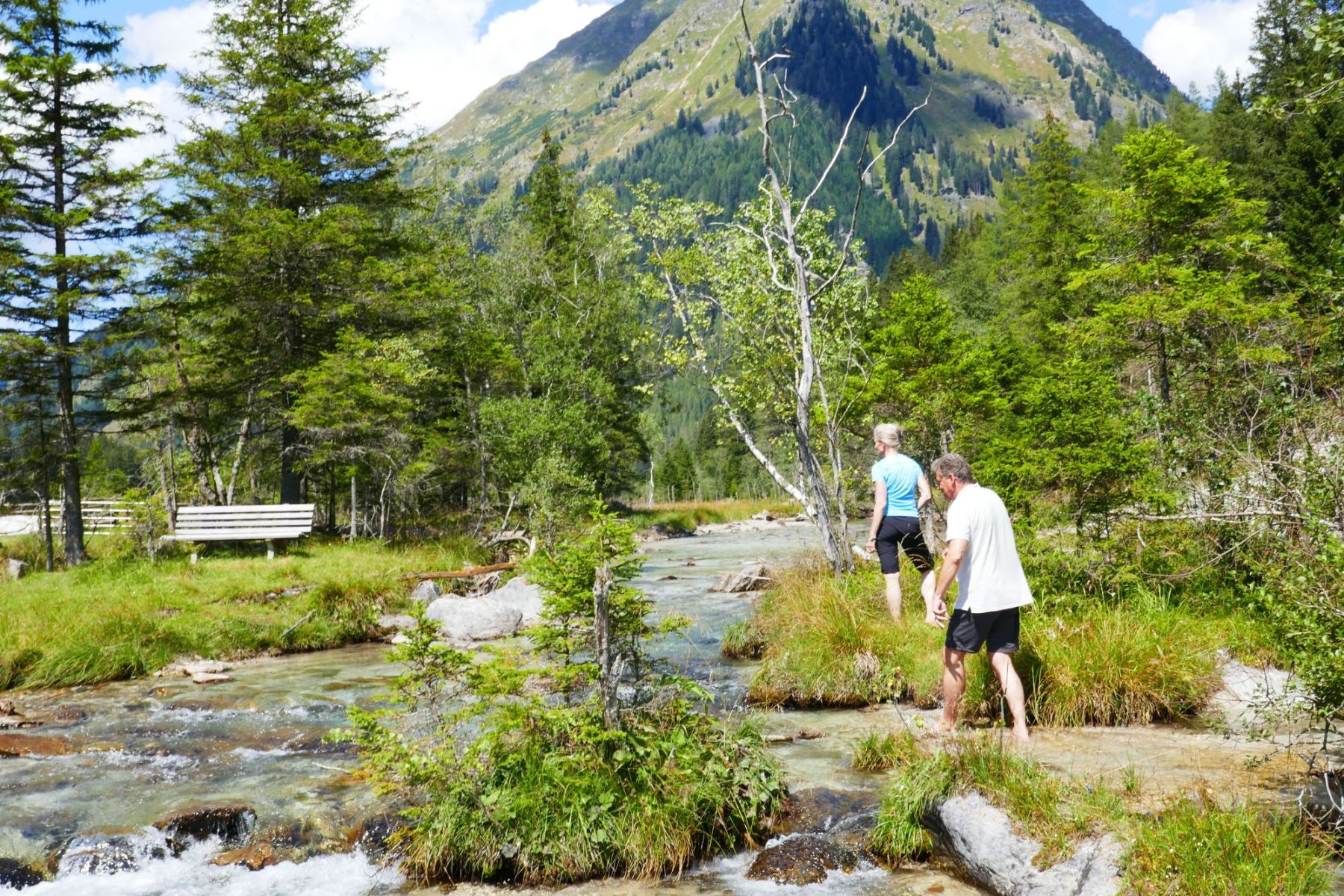Zwei Personen waten in einem seichten Bach, umgeben von üppigem Grün und Bergen im Salzburger Lungau.