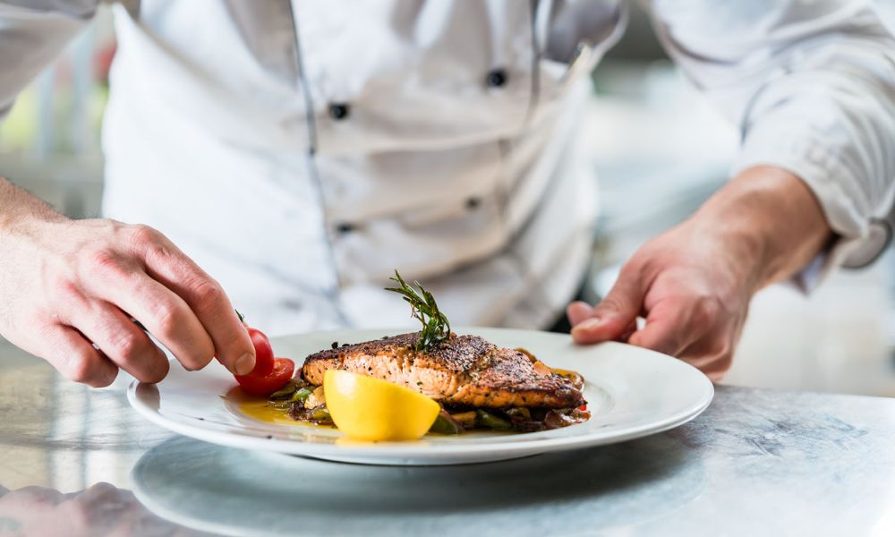 Koch garniert ein Lachsgericht mit Cherrytomaten und Zitrone im Restaurant einer Familienpension.