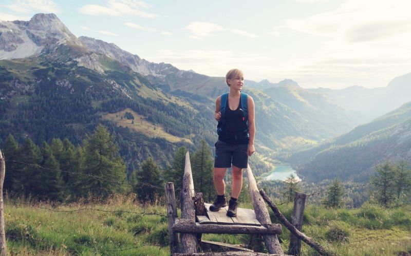 Wanderer auf einer Holzplattform inmitten von malerischen Bergen und Kiefern.