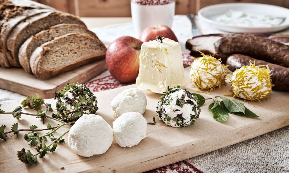 Rustikales Holzbrett mit verschiedenen Käsesorten, Brot, Äpfeln und Würsten, typisches österreichisches Frühstück.