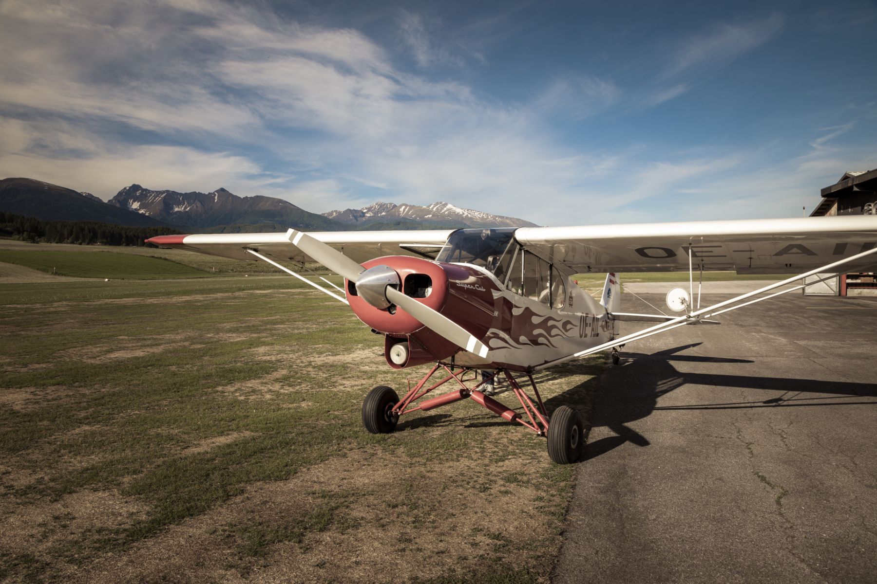 Kleines rotes Flugzeug auf einem Flugfeld, im Hintergrund Berge.