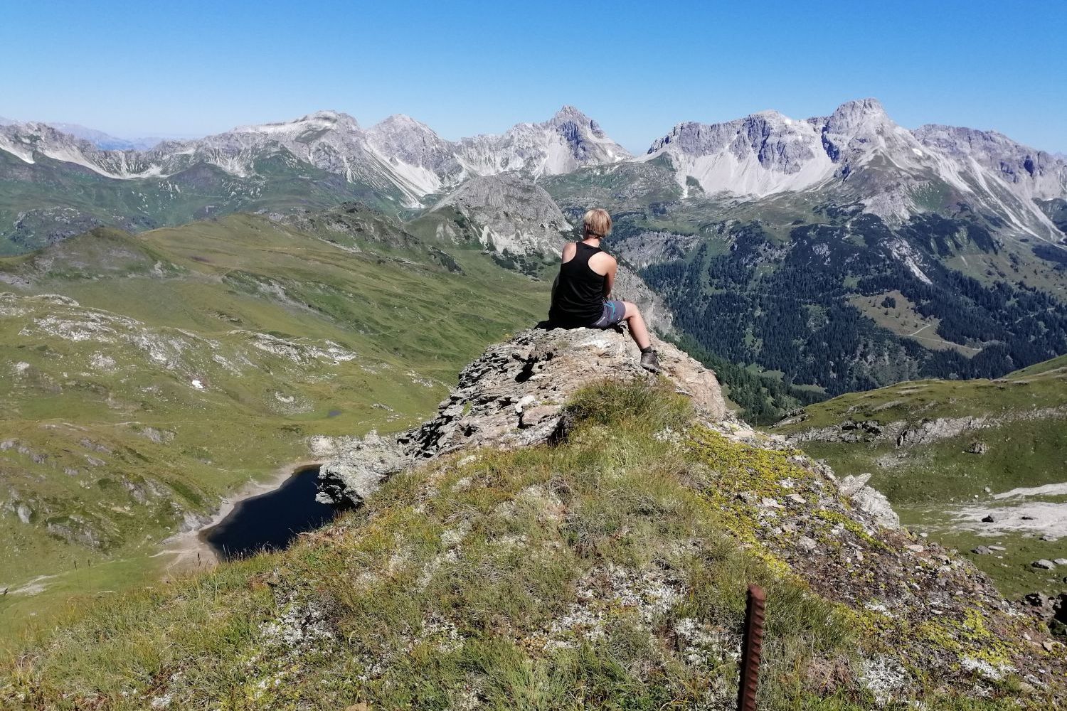 Person sitting on a mountain ledge overlooking a lush valley with distant peaks in Lungau, Salzburg.