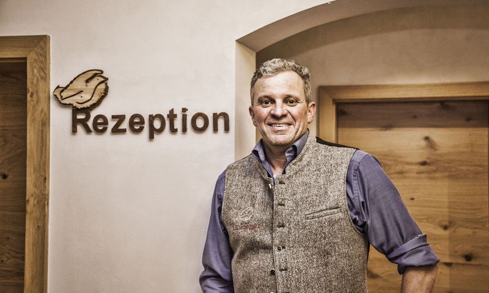 Mann steht neben Holzschild der Rezeption in Familienpension.