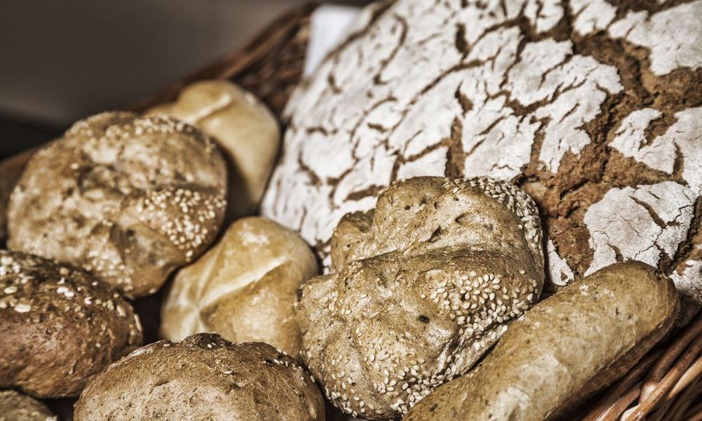 Verschiedene frische Semmeln und ein Laib rustikales Brot mit rissiger Kruste im Korb.