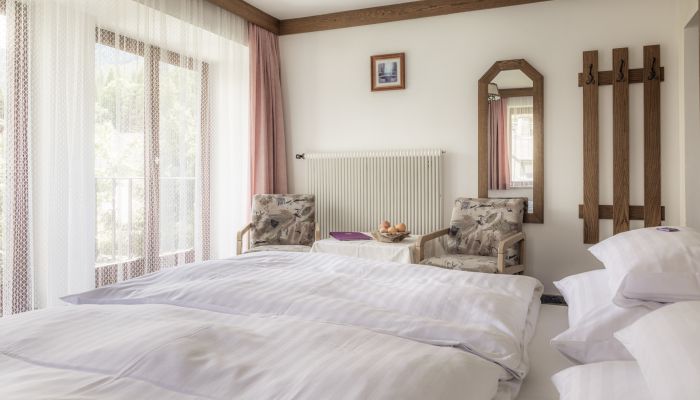 Gemütliches Familienpension-Zimmer mit Doppelbett, Sesseln und Bergblick. Helle Einrichtung und Holzakzente.