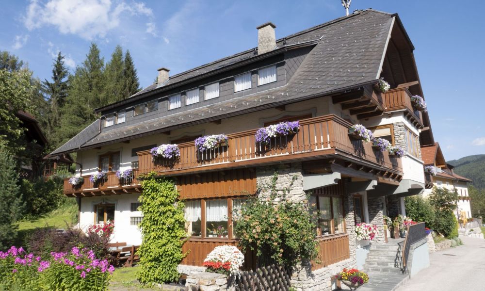 Charmante Alpenpension mit Holzbalkonen und bunten Blumen, eingebettet in die Berge des Salzburger Lungau.
