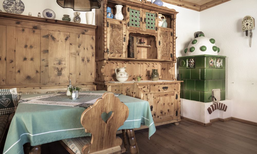 Gemütlicher Innenraum einer österreichischen Pension mit Holzmöbeln und traditionellem grünen Kachelofen.